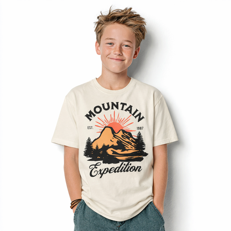 Garçon portant le t-shirt enfant Mountain Expedition écru, badge montagne orange et sapins noirs