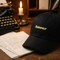 Casquette dad hat noire brodée Amour posée sur un bureau d'écrivain avec des lettres d'amour et une machine à écrire - CHT'M Boutique