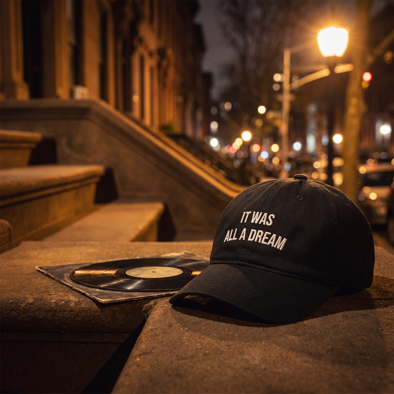 Casquette baseball noire brodée IT WAS ALL A DREAM en blanc sur deux lignes posée sur le perron d'une brownstone de Brooklyn la nuit avec la lueur d'un lampadaire et un vinyle à côté - CHT'M Boutique