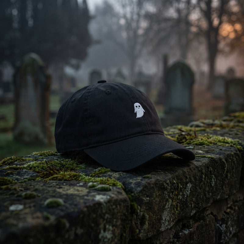 Casquette baseball noire brodée d'un petit fantôme blanc posée sur un muret de pierre moussu dans un cimetière brumeux au crépuscule - CHT'M Boutique