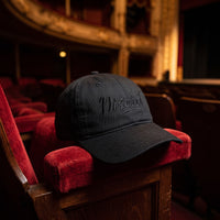 Casquette baseball noire brodée Discret en noir sur noir posée sur l'accoudoir d'un siège en velours rouge dans un théâtre sombre et vide - CHT'M Boutique