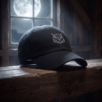 Casquette baseball noire brodée d'une tête de hibou origami géométrique blanche posée sur une poutre de grange la nuit avec la pleine lune derrière une fenêtre, lumière argentée - CHT'M Boutique