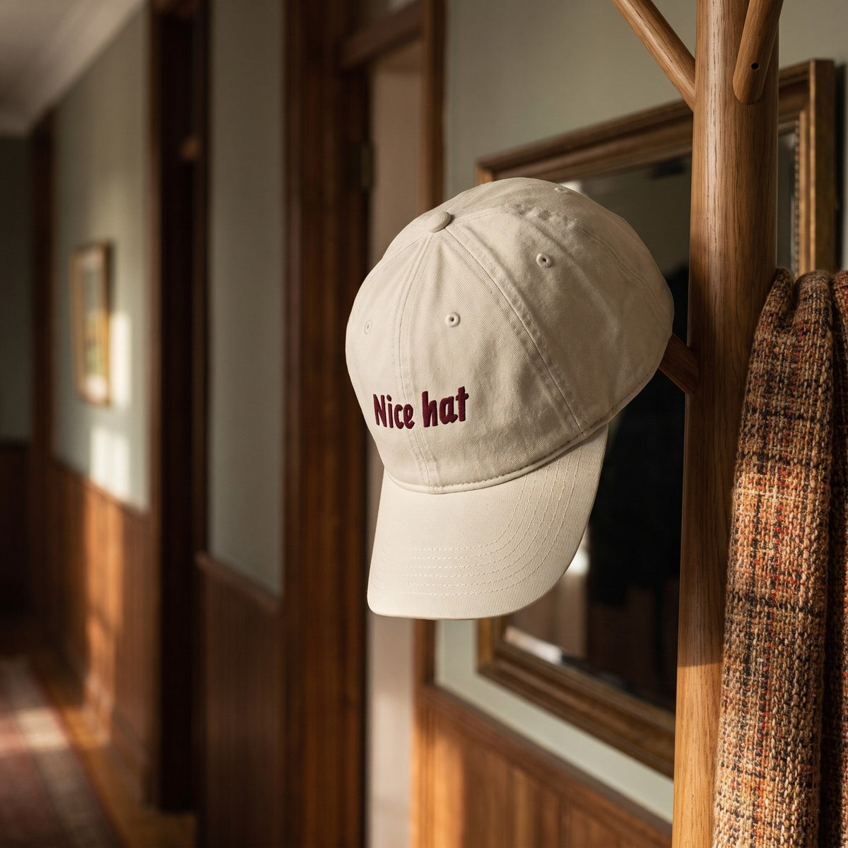 Casquette baseball oyster brodée Nice hat en bordeaux foncé italique posée sur un porte-manteau dans un couloir élégant avec un miroir et une écharpe, lumière douce - CHT'M Boutique