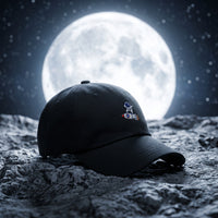 Casquette baseball noire brodée d'un petit astronaute avec le logo Cht'm posée sur une surface rocheuse lunaire devant une immense pleine lune et des étoiles, lumière nocturne cinématographique - CHT'M Boutique