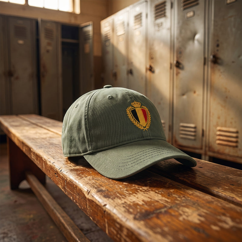 Casquette belge vintage verte avec blason doré posée sur un banc dans un vestiaire de foot vintage - CHT'M Boutique