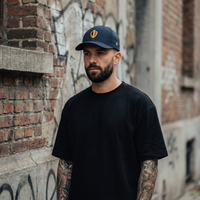 Homme portant la casquette belge Flexfit bleu marine au blason belge brodé fil doré, ambiance streetwear à Bruxelles