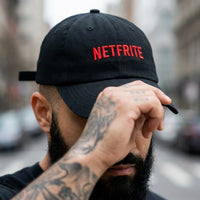 Gros plan sur la broderie rouge NETFRITE de la casquette belge portée par un homme tatoué