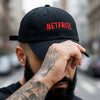 Gros plan sur la broderie rouge NETFRITE de la casquette belge portée par un homme tatoué