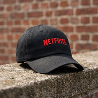 Casquette originale NETFRITE noire posée sur un muret – vue trois quarts, visière courbée