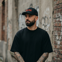 Homme portant la casquette belge noire Flexfit, mot BELGE brodé fil rouge, streetwear à Bruxelles