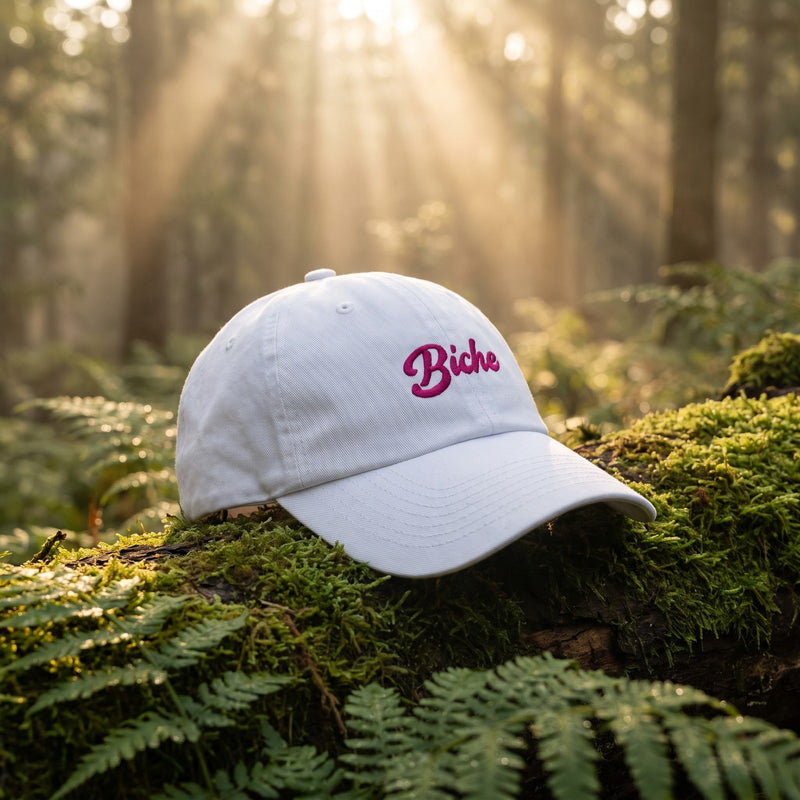 Casquette dad hat blanche brodée « Biche » posée sur une bûche moussue dans une clairière brumeuse à l'aube - CHT'M Boutique