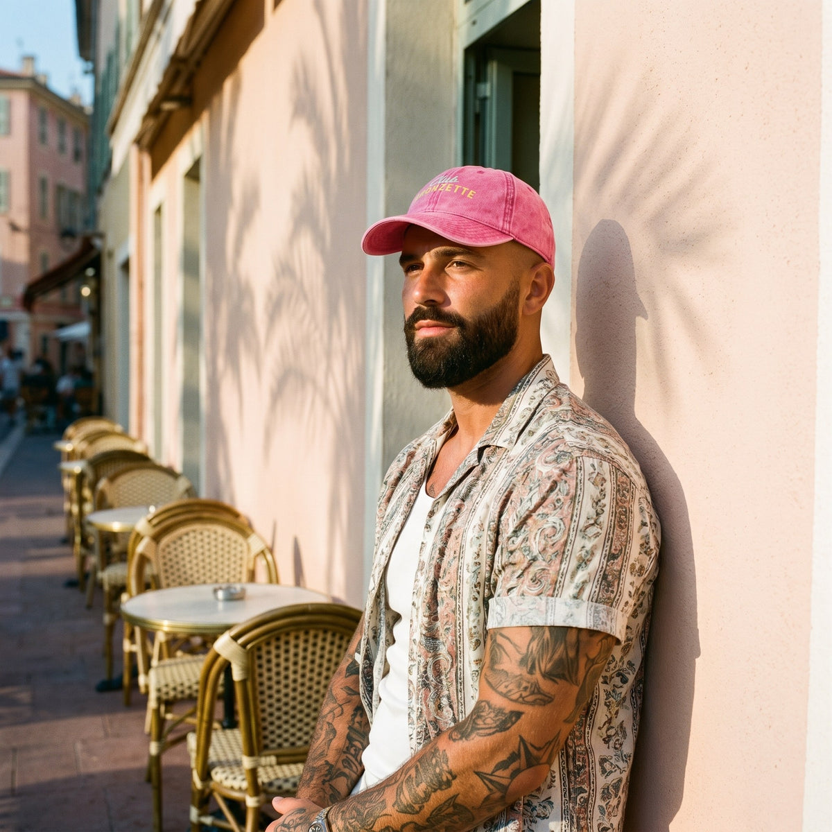 Casquette bronzette vintage rose portée par un homme tatoué en terrasse, ambiance riviera urbaine streetwear