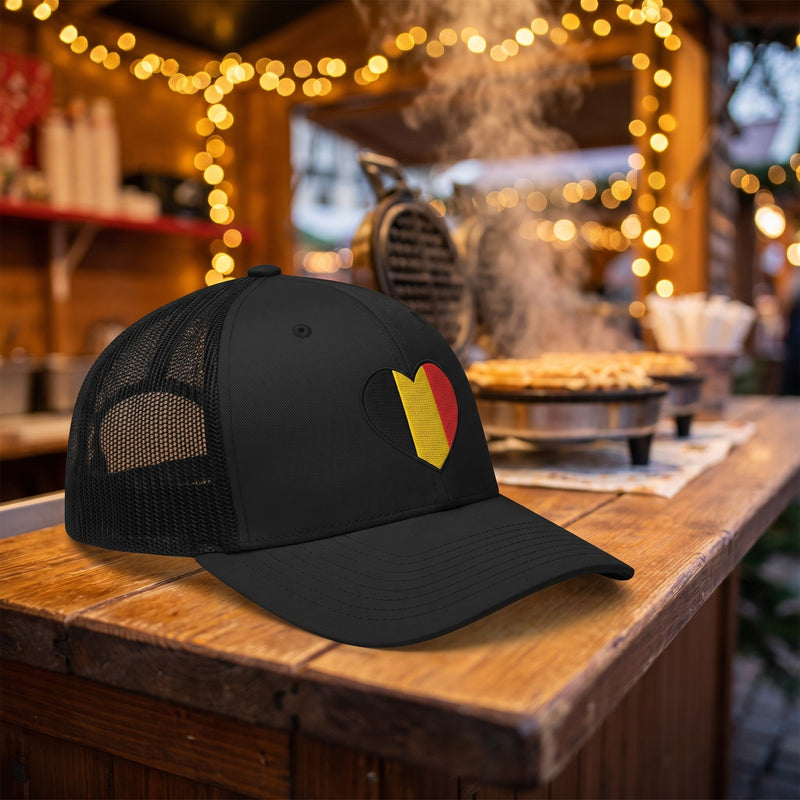 Casquette trucker noire brodée cœur belge posée sur le comptoir d'un stand de gaufres au marché de Noël - CHT'M Boutique