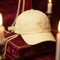 Casquette jaune pastel brodée Diamond doré posée sur un coffret à bijoux ancien en velours avec un collier de perles - CHT'M Boutique