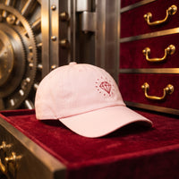 Casquette rose pastel brodée Diamond rouge posée dans un coffre-fort ouvert avec des tiroirs en velours - CHT'M Boutique