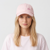 Femme blonde portant la casquette femme rose pastel brodée oiseau, fond clair