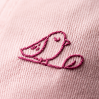 Macro de la broderie oiseau fil rose sur la casquette pastel
