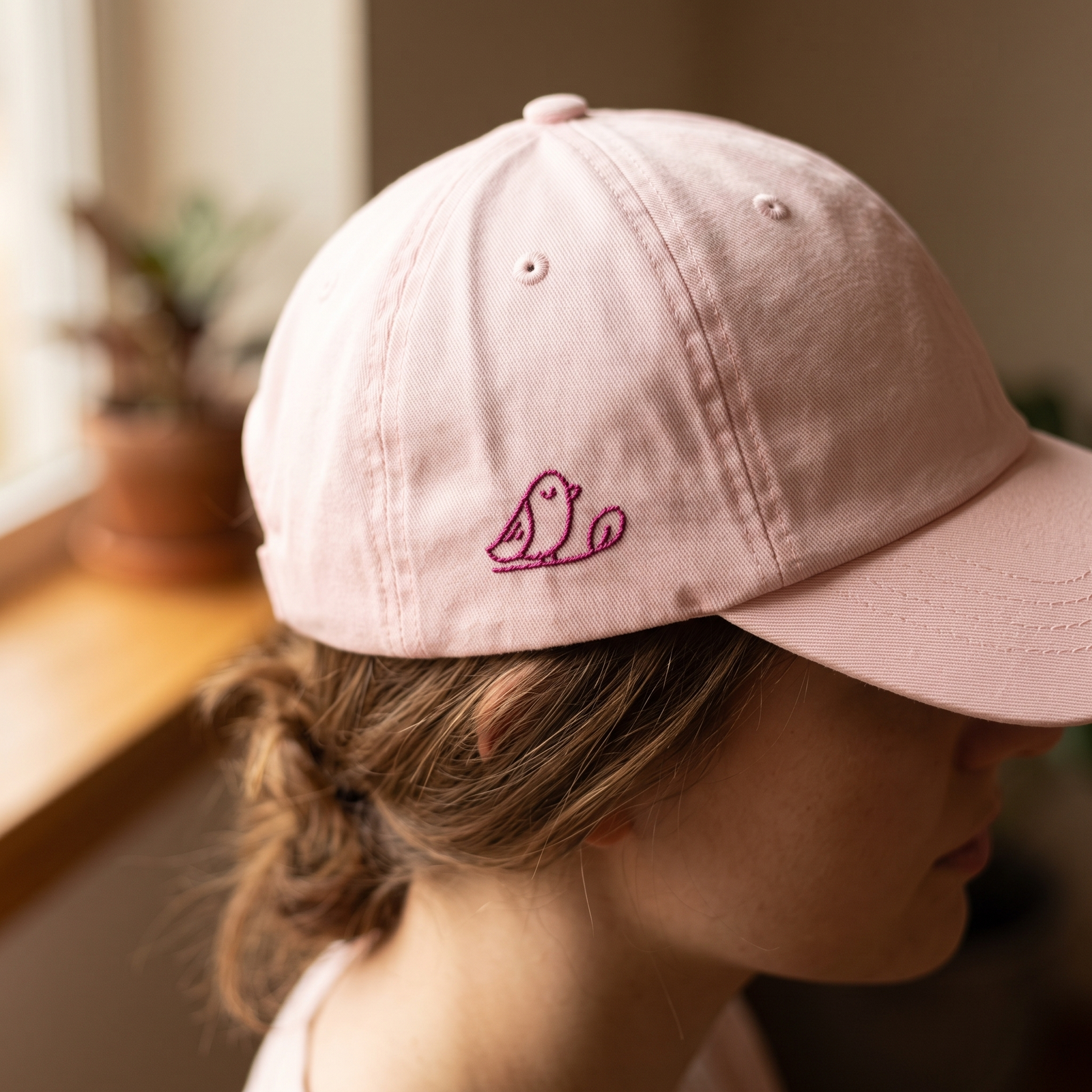 Détail de la broderie oiseau sur la casquette rose pastel portée