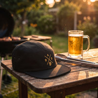 Casquette 5 panneaux noire brodée DAD avec une chope de bière dorée posée sur une table de barbecue au jardin avec une bière fraîche et des pinces - CHT'M Boutique