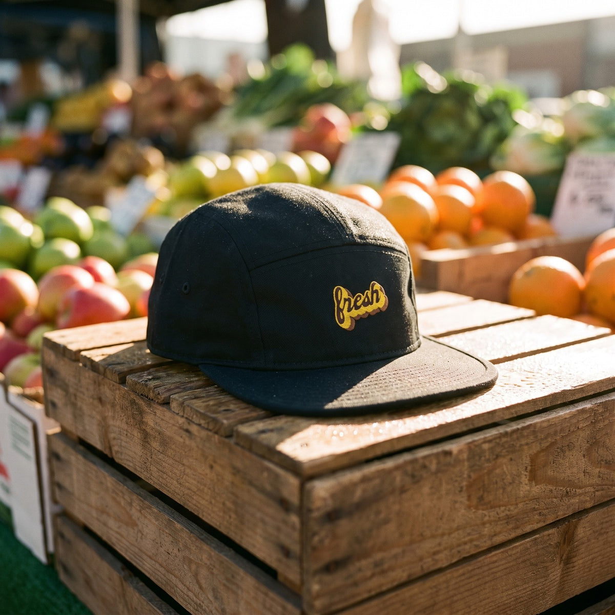Casquette 5 panneaux noire brodée fresh en jaune posée sur des cageots à un étal de fruits et légumes au marché - CHT'M Boutique