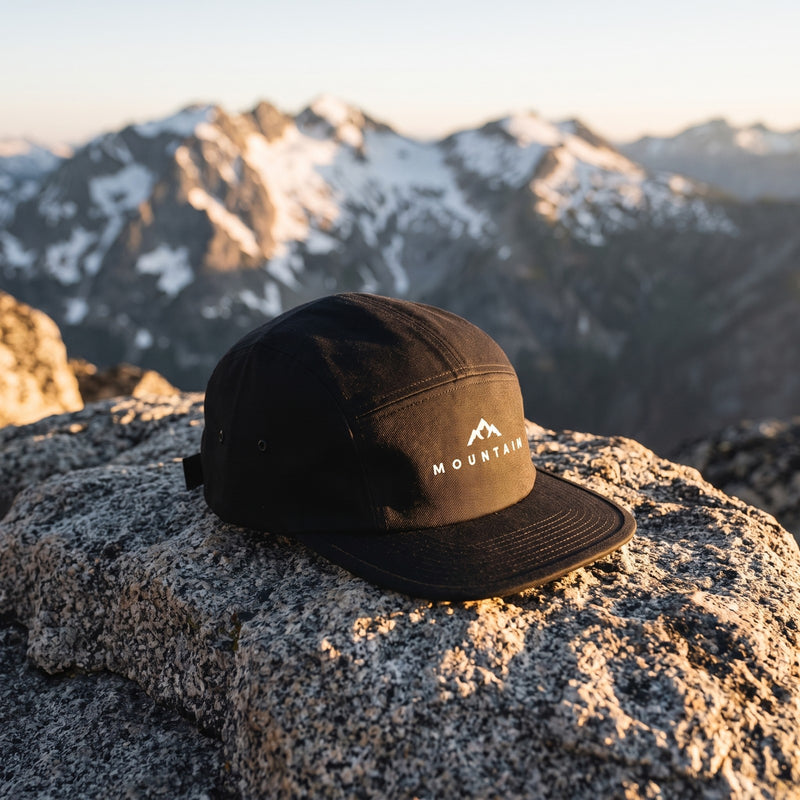 Casquette 5 panneaux noire brodée MOUNTAIN avec un sommet de montagne posée sur un rocher de granit au sommet d'une montagne face aux pics enneigés - CHT'M Boutique