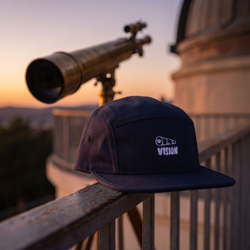Casquette 5 panneaux bleu marine brodée VISION avec une longue-vue blanche posée sur la rambarde d'une terrasse d'observatoire au crépuscule à côté d'un télescope en laiton - CHT'M Boutique