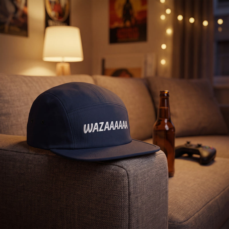 Casquette 5 panneaux bleu marine brodée WAZAAAAAA en blanc posée sur l'accoudoir d'un canapé avec une bouteille de bière et une manette de jeu - CHT'M Boutique