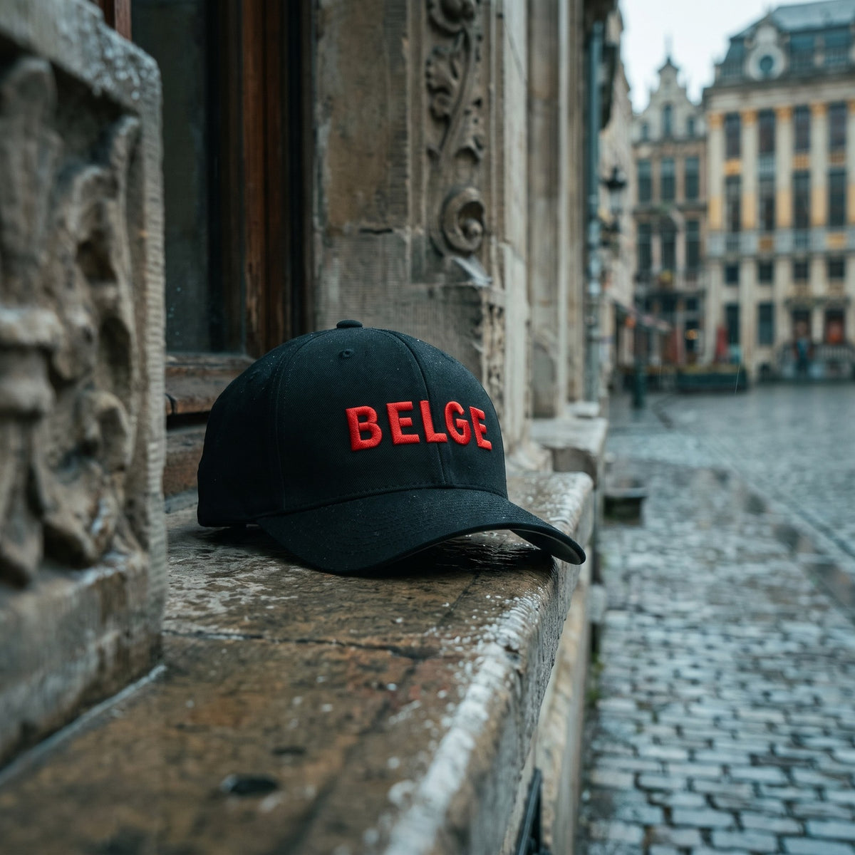 Casquette Flexfit noire brodée BELGE rouge posée sur le rebord en pierre d'une maison Art nouveau à Bruxelles sous la pluie - CHT'M Boutique