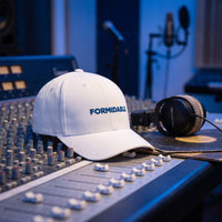 Casquette Flexfit fermée à l'arrière blanche brodée FORMIDABLE en bleu posée sur une console de mixage dans un studio d'enregistrement à côté d'un casque audio et d'un vinyle - CHT'M Boutique