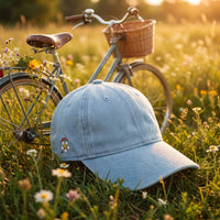Casquette denim bleu clair brodée Flower Power posée dans une prairie de fleurs sauvages à côté d'un vélo vintage - CHT'M Boutique