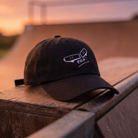 Casquette baseball noire brodée FVCK posée sur le bord en bois d'une mini rampe au coucher du soleil - CHT'M Boutique