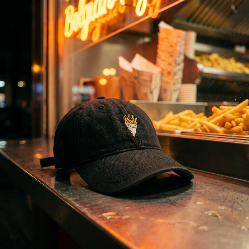 Casquette belge en jean noir brodée d'un cornet de frites posée sur le comptoir d'une friterie belge la nuit - CHT'M Boutique