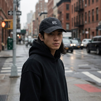Portrait d'un homme en hoodie noir portant la casquette NYC en denim noir délavé, rue de New York sous la pluie, style streetwear