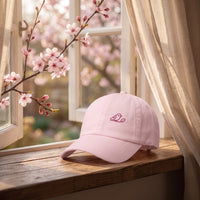 Casquette dad hat rose pastel brodée oiseau du paradis posée sur un rebord de fenêtre avec des branches de cerisier en fleurs - CHT'M Boutique