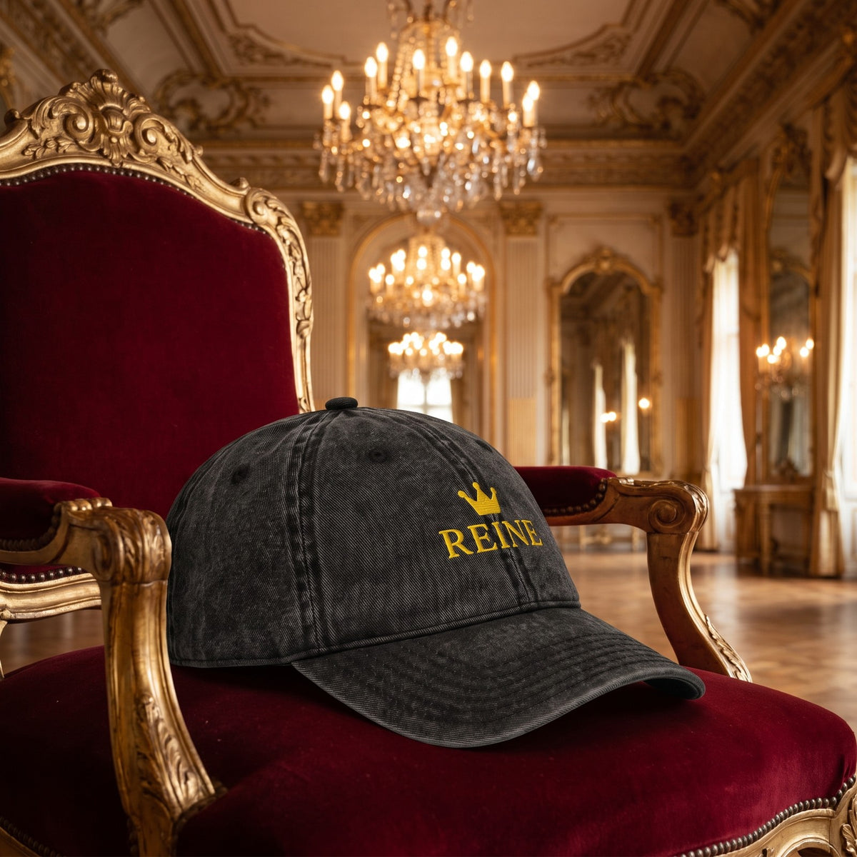 Casquette vintage délavée noire brodée Reine avec couronne dorée posée sur un trône de velours rouge dans une salle de bal baroque vide - CHT'M Boutique
