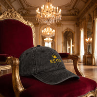 Casquette vintage délavée noire brodée Reine avec couronne dorée posée sur un trône de velours rouge dans une salle de bal baroque vide - CHT'M Boutique