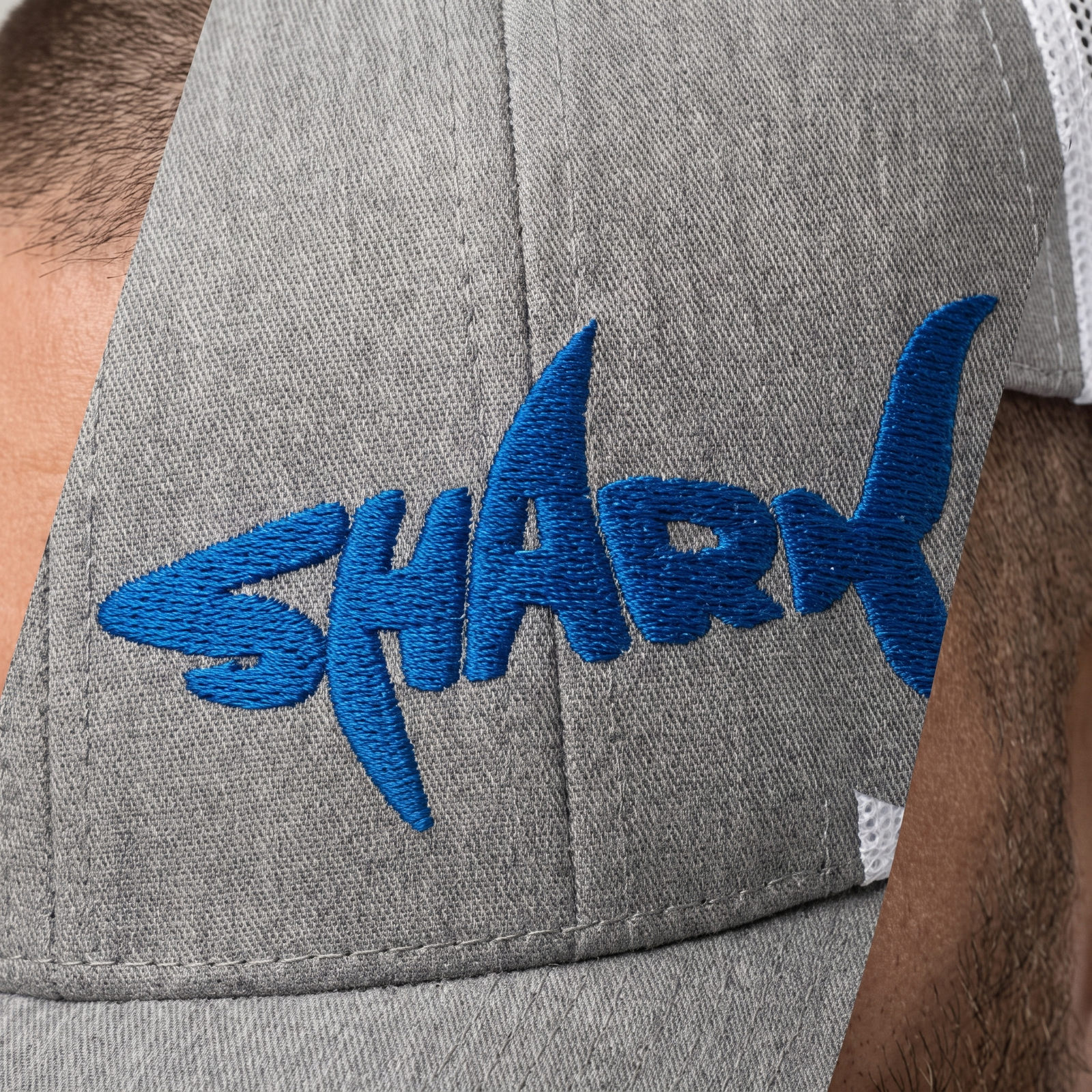 Gros plan du design requin SHARK brodé bleu roi sur le panneau avant de la casquette portée