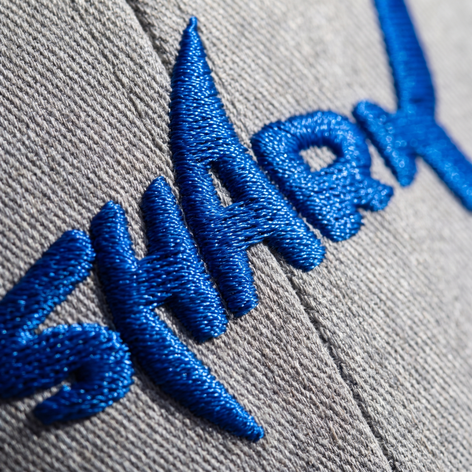 Macro de la broderie bleu roi en relief du logo requin SHARK sur tissu gris chiné
