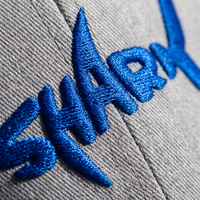 Macro de la broderie bleu roi en relief du logo requin SHARK sur tissu gris chiné