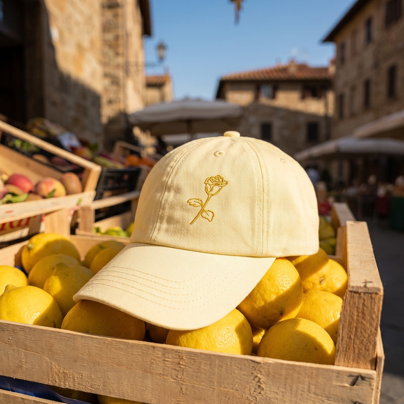 Casquette baseball jaune pastel brodée d'une rose posée sur une caisse de citrons à un étal de marché italien - CHT'M Boutique