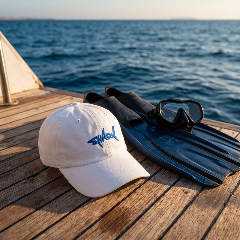 Casquette dad hat blanche brodée Shark posée sur le pont d'un bateau de plongée à côté de palmes et d'un masque - CHT'M Boutique
