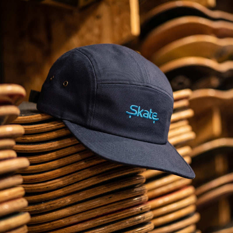 Casquette skate 5 panneaux bleu marine brodée Skate posée sur un mur de planches de skate dans un skate shop - CHT'M Boutique