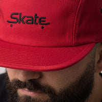 Gros plan sur la broderie Skate noire de la casquette 5 panneaux rouge portée