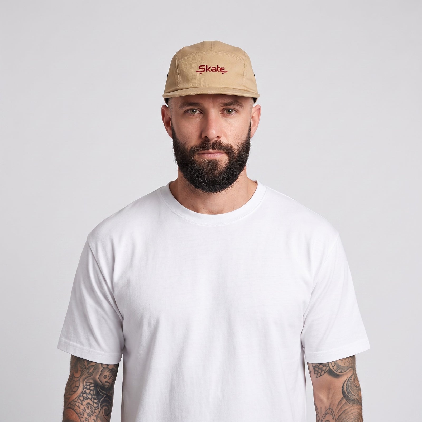 Homme barbu tatoué portant la casquette skate brodée 5 panneaux beige – photo studio
