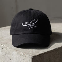 Casquette skate brodée FVCK noire posée sur béton, design skateboard cassé complet vu de face