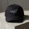 Casquette skate brodée FVCK noire posée sur béton, design skateboard cassé complet vu de face