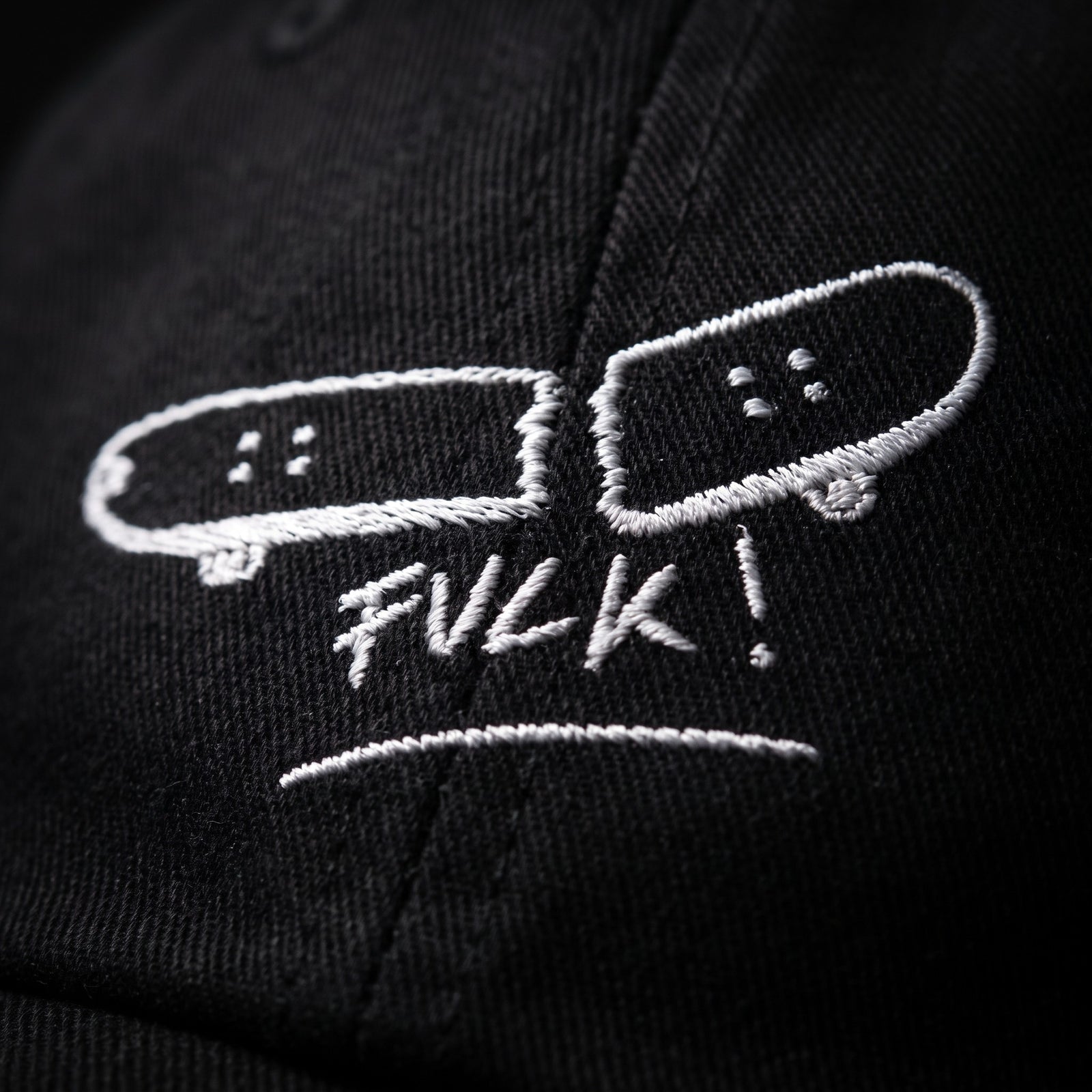 Macro de la broderie blanche skateboard cassé FVCK sur sergé de coton noir