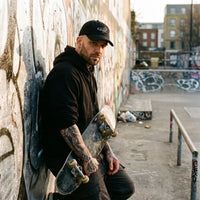 Skateur tatoué en rue portant la casquette skate brodée FVCK noire, ambiance streetwear urbain