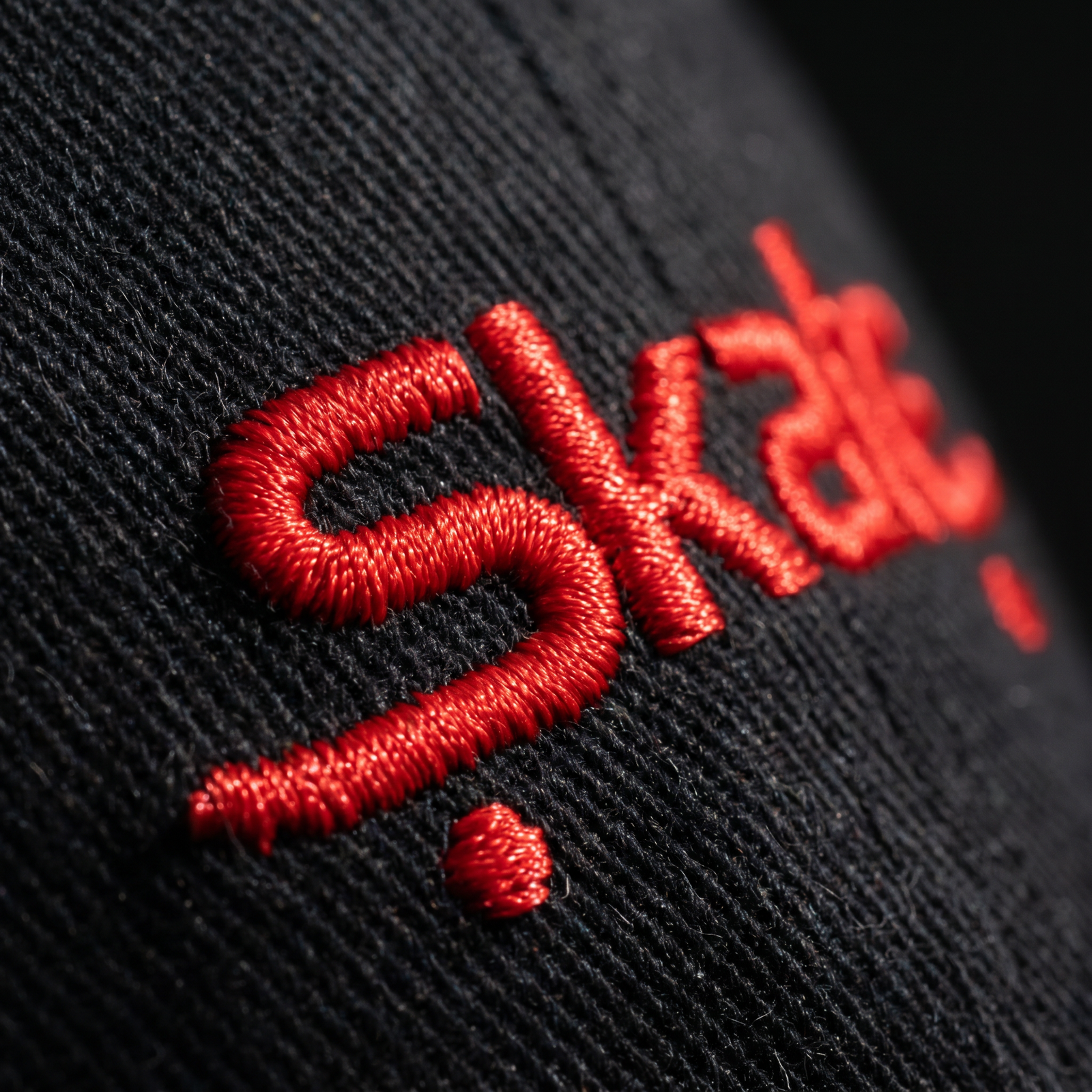 Macro de la broderie fil rouge Skate sur le coton chino noir de la casquette