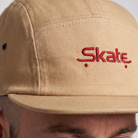 Gros plan sur la broderie rouge Skate de la casquette 5 panneaux beige portée